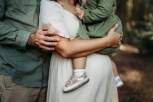 close up on a mom holding her toddler on her baby bump. dads hand is on moms arm