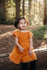 little girl laughs at camera while sitting on a fallen redwood