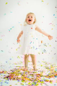 little girl yells and has arms wide as she happily watches confetti fall
