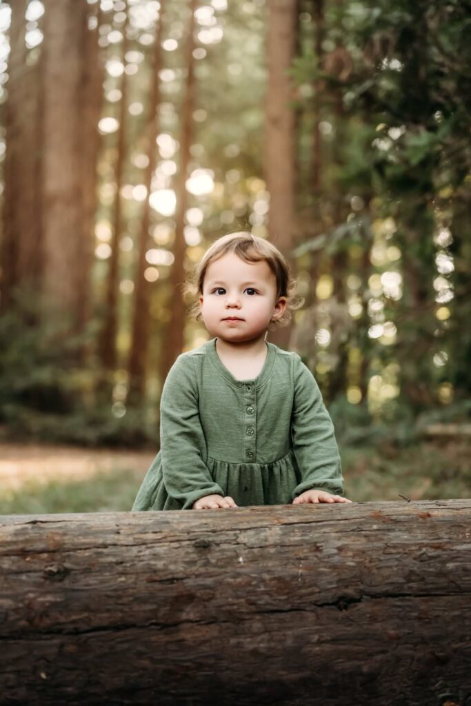 Young child standing behind a fallen log in a forest setting during an outdoor family photo session in the East Bay.