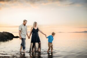 Family of three walking hand in hand across a sandy trail during a glowing East Bay beach sunset.
