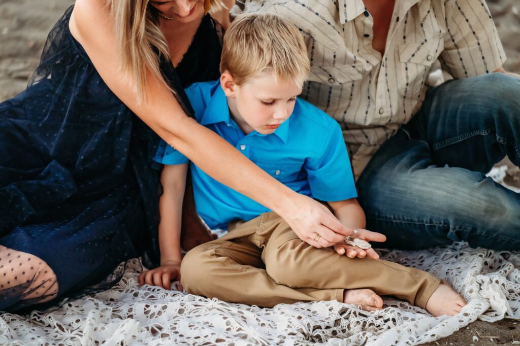 Child examining a seashell while sitting with parents during a calm beach moment.