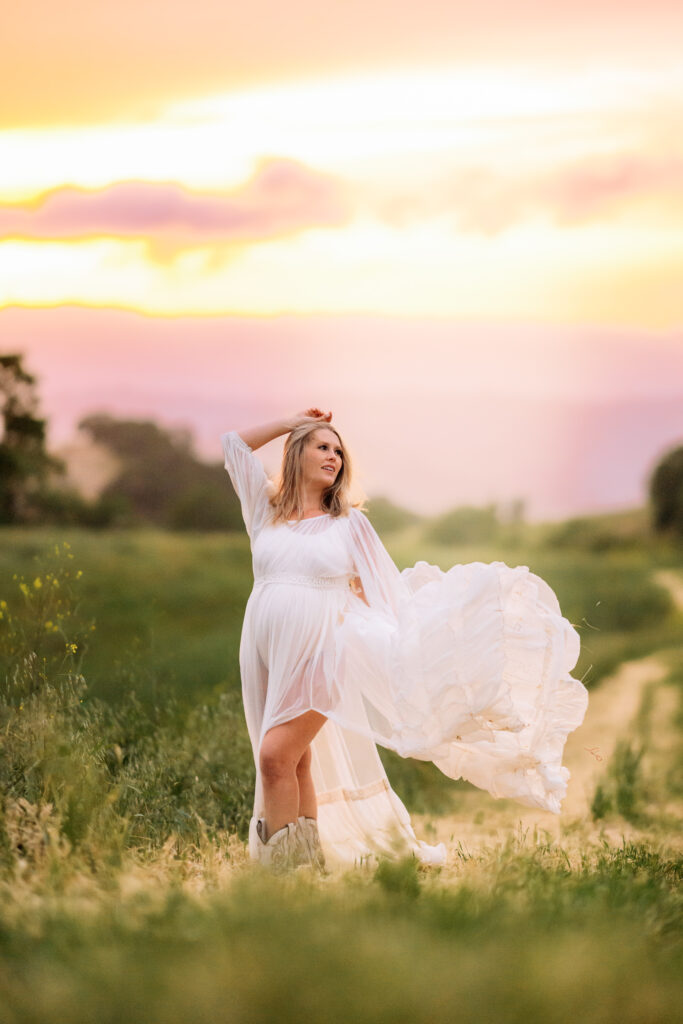 pregnant mom in white flowy maternity gown that is blown by the wind