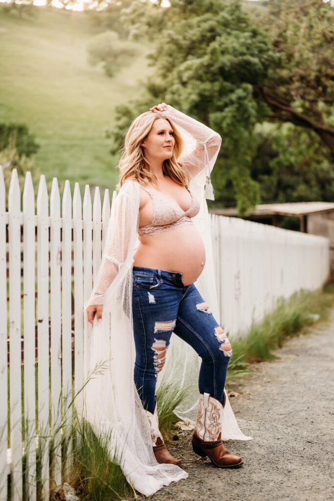pregnant mom against a fence at borges ranch with jeans and cowboy boots