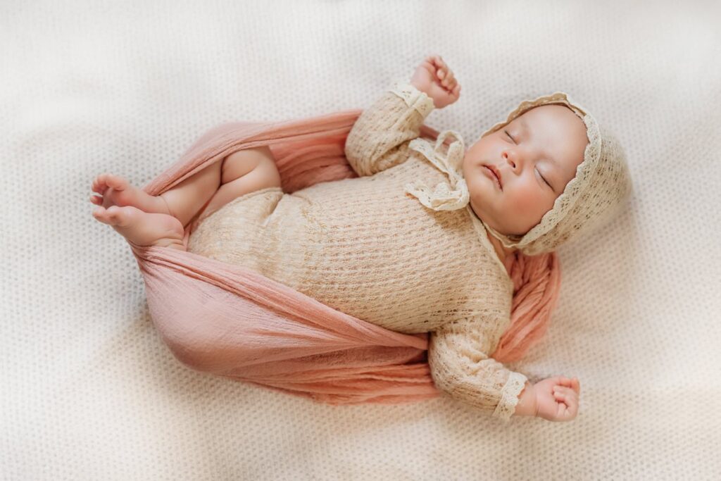 newborn girl in a tan knit romper circled by a pink swaddle