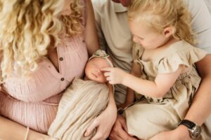 newborn photo where sibling is touching her baby sisters nose