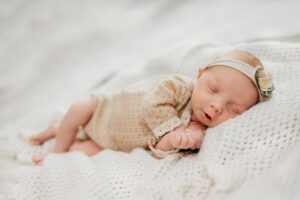 newborn on her side in a knit romper and floral bow on her head