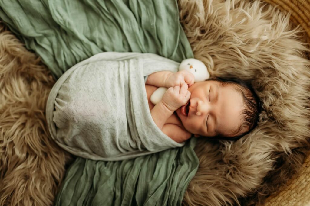 sleepy newborn with hands poking out of wrap on a fluffy furry blanket