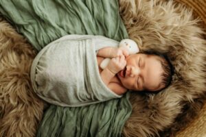 sleepy newborn with hands poking out of wrap on a fluffy furry blanket