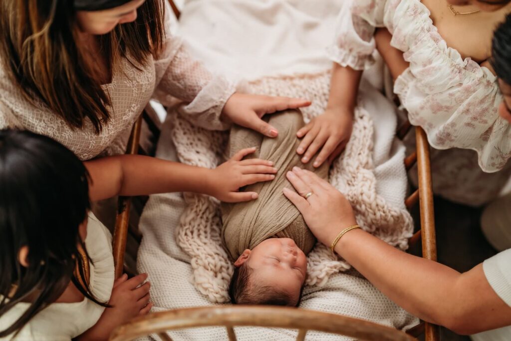 newborn boy in vintage crib with his parents and sisters hands resting on him