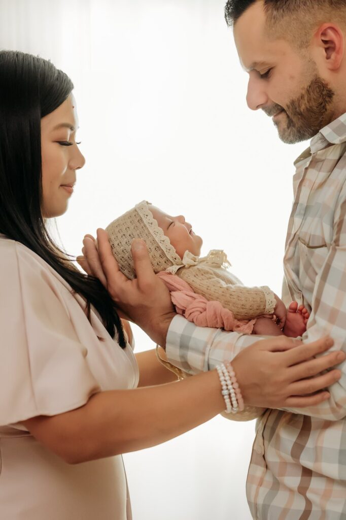 studio lit new family with their sleeping newborn girl between them. she slightly smiles