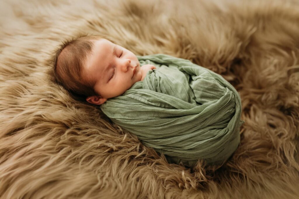 newborn in a studio setting wrapped in a green swaddle on a fuzzy blanket