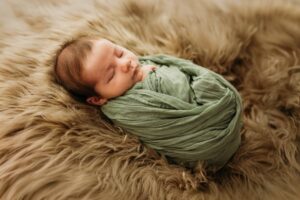 newborn in a studio setting wrapped in a green swaddle on a fuzzy blanket