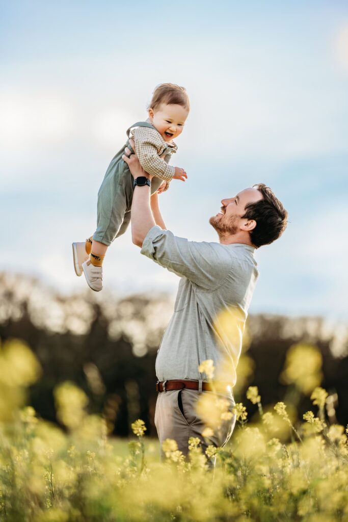 dad lifts baby up in a field of pale yellow flowers