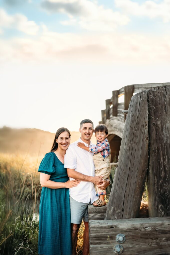 toddler stands on a post of the martienz bridge near his parents as everyone looks at the camera and smiles