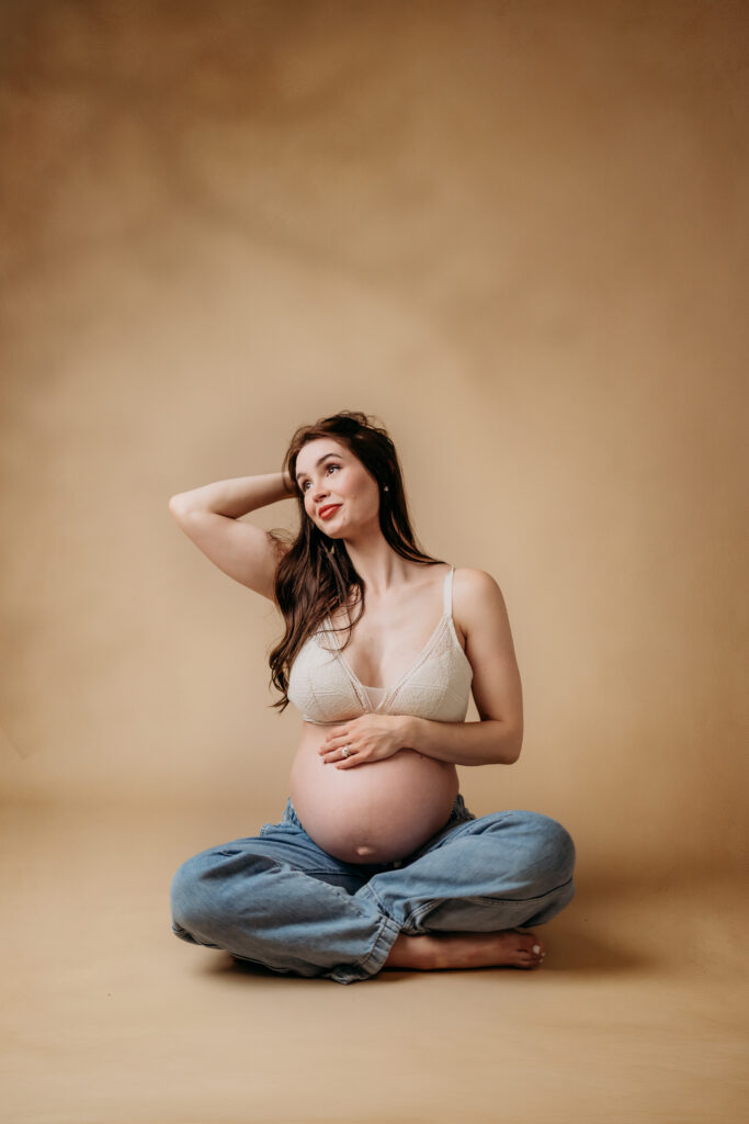 pregnant mama in tan studio setting with slight shadows behind her