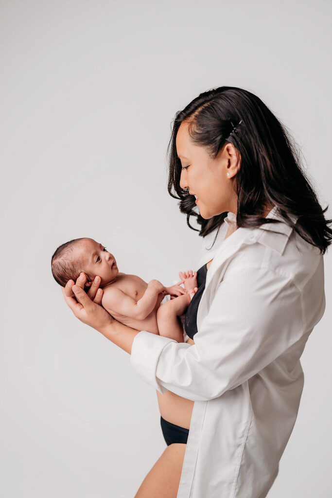 same mama in same white maternity shirton same white studio backdrop but now she holds her newborn baby