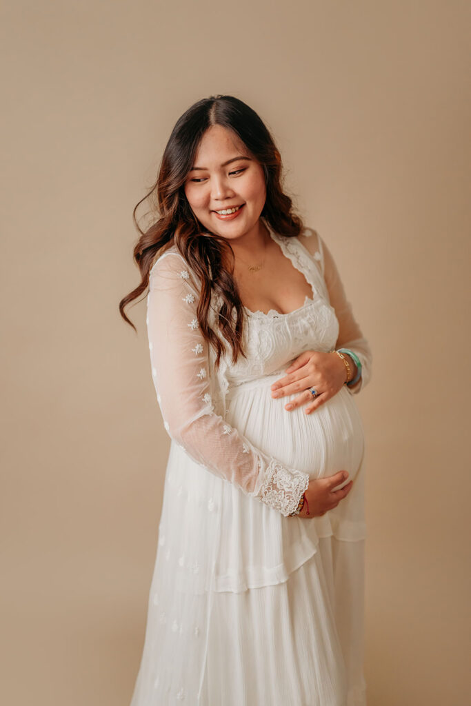 pregnant mama on a simple tan studio backdrop holding her pregnant belly.