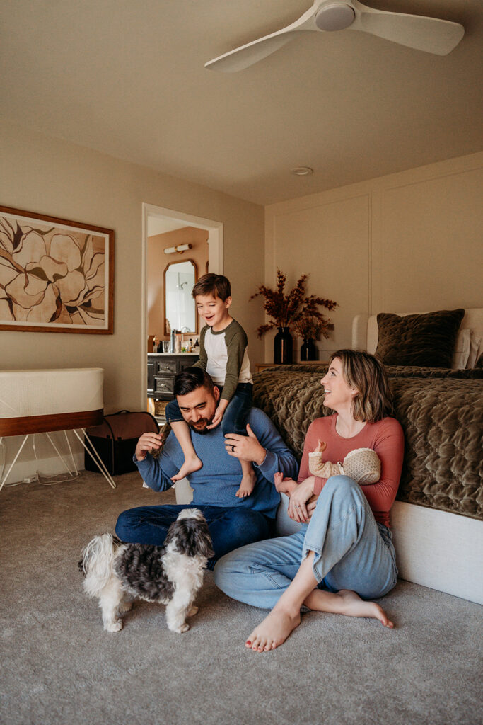 toddler on dads shoulders while mom holds their newborn baby in their home