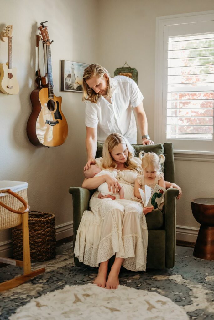 family of 4 in their newborn babys nursery. the toddler reads a book on moms lab