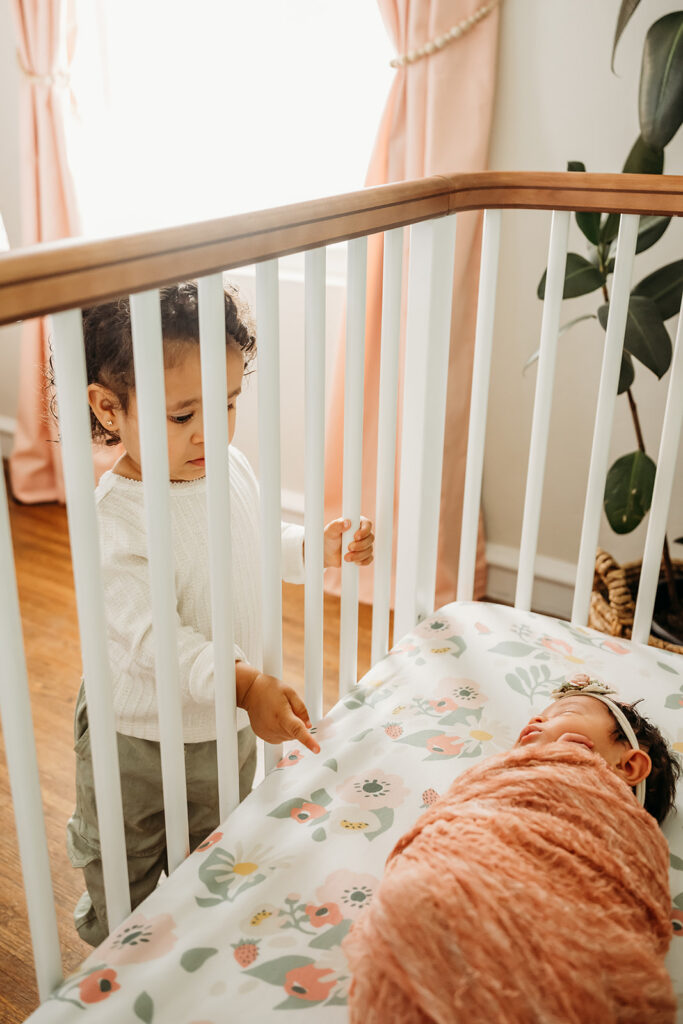toddler peeks into her baby sisters crib during their photography session